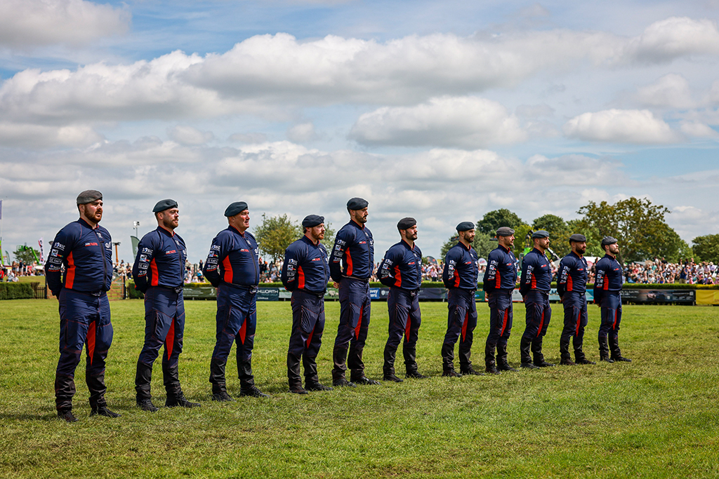 Eleven RAF Falcons stand together in their red trimmed dark blue jumpsuits after saluting the crowd, having landed on the designated area of the showground